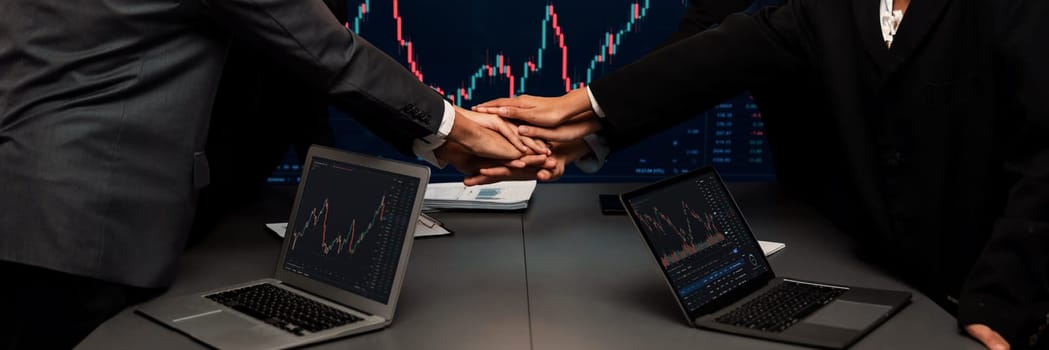 Stock investor put hand stack together over meeting table as synergy teamwork after made successful financial data analysis on stock graph and strategic planning for stock trading. Trailblazing