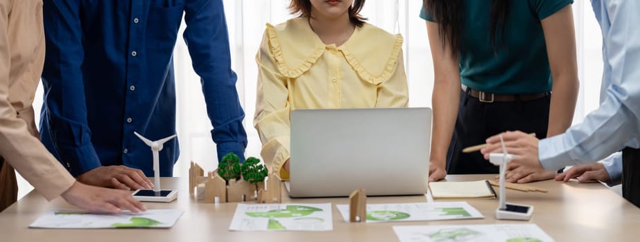 Professional business team prepare to present green business on table with windmill presented using renewable energy, wooden block and environmental document scatter around. Closeup. Delineation.