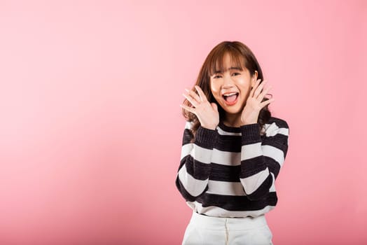 Portrait of an exuberant Asian woman making a success gesture with raised fists, expressing excitement. Studio shot isolated on pink background, radiating joy and happiness.