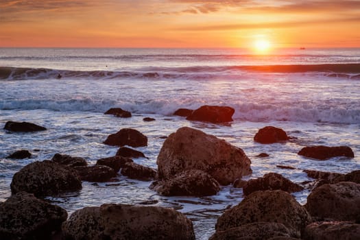 Atlantic ocean sunset with waves and rocks at Costa da Caparica, Portugal
