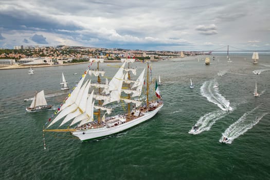 Aerial drone view of tall ships with sails sailing in Tagus river towards the Atlantic ocean in Lisbon, Portugal