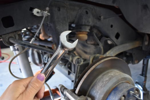 Female Hand with Purple Nail Polish holding a Wrench by car, working on Car with Tire Off. High quality photo