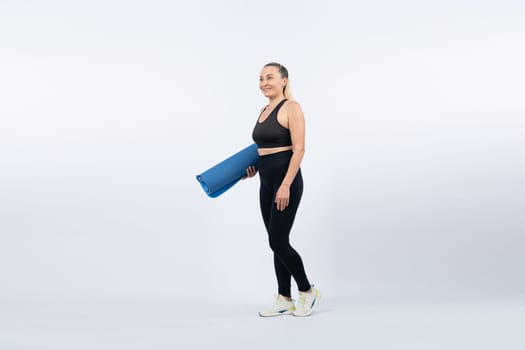 Full body length shot athletic and sporty senior woman holding fitness exercising mat on isolated background. Healthy active physique and body care lifestyle after retirement. Clout