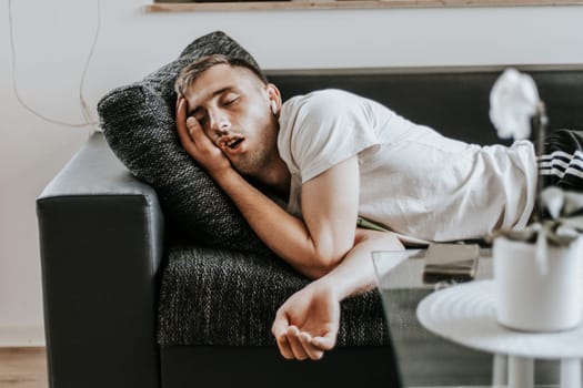 One young Caucasian handsome guy sleeps soundly with his mouth open while lying on the sofa in the salon on a summer day, close-up side view in slow motion.