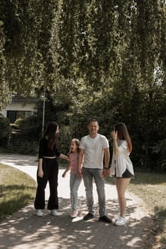 Portrait of a young beautiful Caucasian father with his three daughters entertaining and having fun in the park on a summer day, side view.