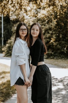 Portrait of two young beautiful Caucasian girls holding hands in a city park on a summer day, side view.