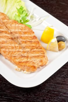 Grilled salmon steak with greens,onion, lemon, lime and olive