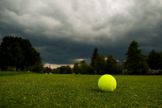 A tennis ball on the lawn in a park, cloudy sky