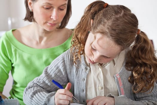 Teenager girl sitting together with her mother and showing her homework