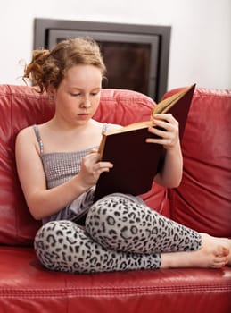 Teenager girl sitting on leather sofa and reading book