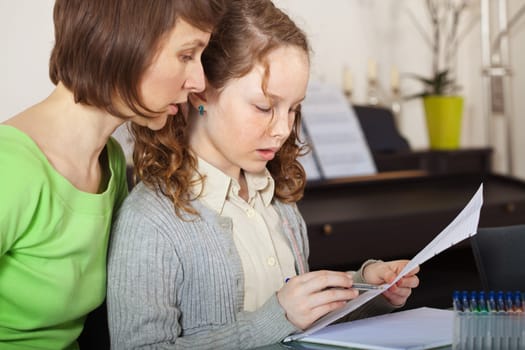 Teenager girl sitting together with her mother and showing her homework
