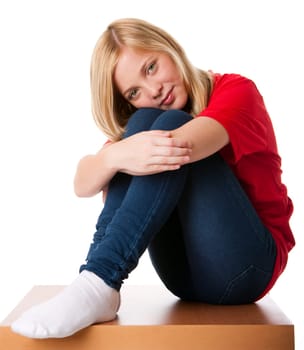Cute teenager girl feeling lonely sitting alone with knees pulled up and arms around legs, isolated.