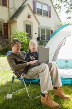 Father and son camping in the front yard with laptop computer