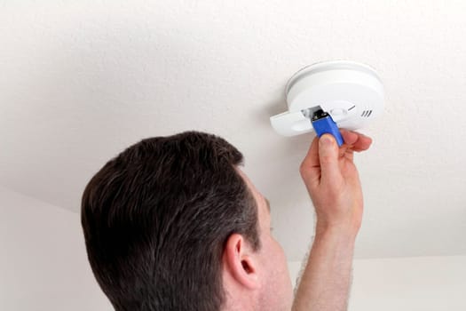 Man changing the 9 volt battery in a round white ceiling smoke alarm detector for fire safety.