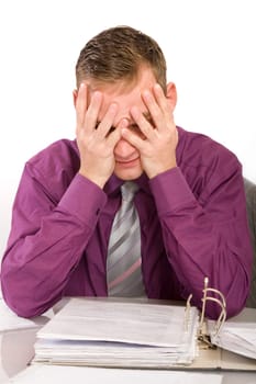 Overwhelmed and desperate businessman in the office. He sits in front of a file folder and holds his hands in front of his face.