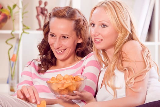 two women with bowl snacks watching television
