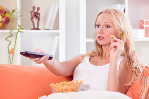woman with remote control and chips watching television on sofa