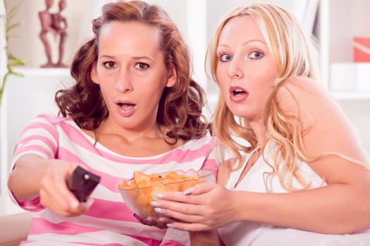 two women friends watching horror movie in living room