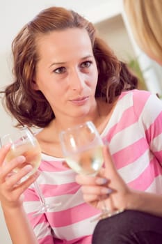 two women friends talking with wine glasses in living room
