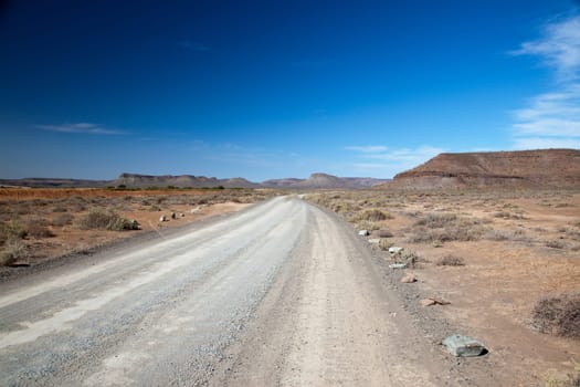 Dry landscape in South Africa with lonely road or highway with a view and bright blue sky - horizontal