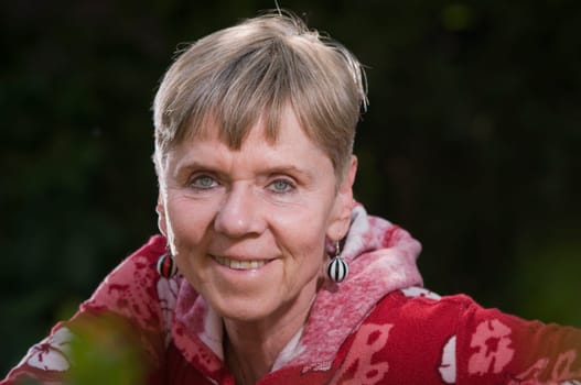 Portrait of an elderly woman on a park bench in summer with her torso turned backwards over the backrest looking towards the camera