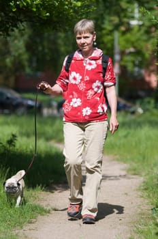 Full length shot of elderly woman with dog on a leash on a path in city park in summer