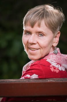 Head and shoulders portrait of a mature woman on a park bench looking over her shoulder backwards over the backrest towards the camera