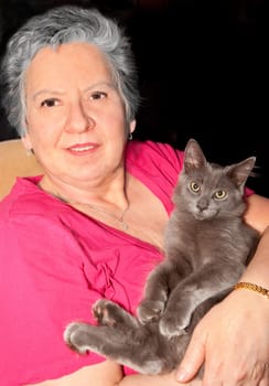 A senior woman is happilly holding a grey cat.