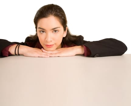A young woman is leaning on a desk while looking at the camera.