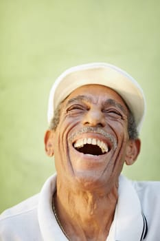 portrait of senior hispanic man with white hat looking up against green wall and smiling. Vertical shape, copy space