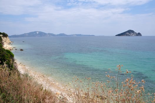 Empty eroded stone beach in Laganas bay Zakynthos, Greece. Distant view of Marathonisi islet natural caretta sea turtle habitat.