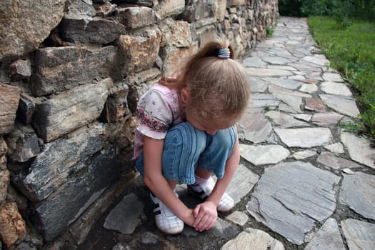 sad little girl sitting in a stone wall and buried her face in her lap
