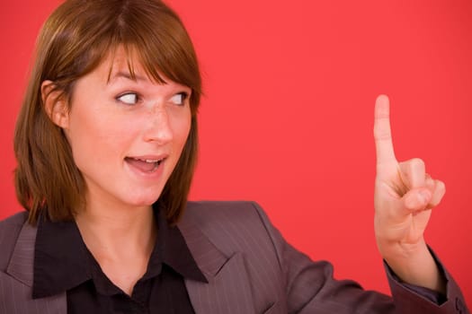 smiling woman gesturing as if she has an idea with raised finger, on red background