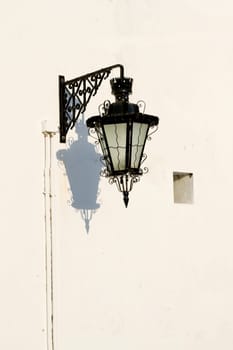 View of an old styled urban street light attached to a white wall.