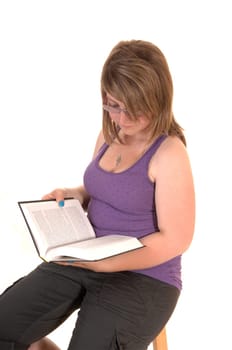Young teenager, sitting on a chair, holding a book in her hands and reading, for white background.