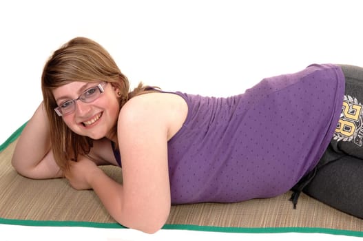 Teenage girl lying on a yoga matt on the floor, resting and having a good time, smiling into the camera, for white background.