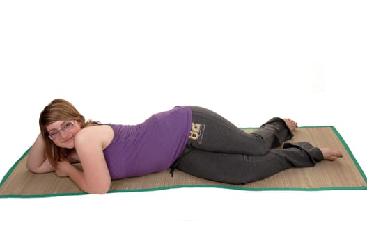 An teenager resting on a yoga matt on the floor, lying down in her track pants and glasses, for white background.