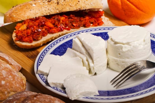 View of a dish of fresh cheese with sandwich of chorizo and fruit.