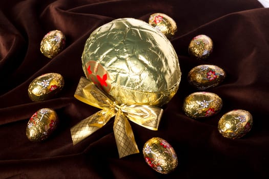 Close up view of sweet golden eggs of chocolate spread on a dark brown silk background.