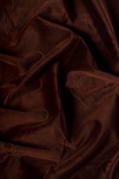 Close up view of a wrinkled dark brown silk fabric background.