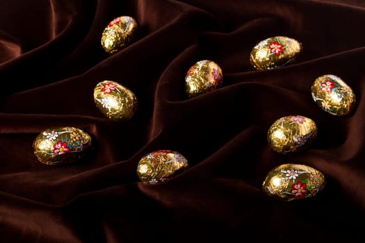 Close up view of sweet golden eggs of chocolate spread on a dark brown silk background.