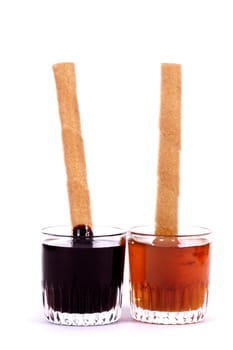 Close up view of a glass of honey and another of chocolate with cookie rolls.