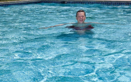 Baby boomer male floating in a backyard swimming pool on a hot summers day