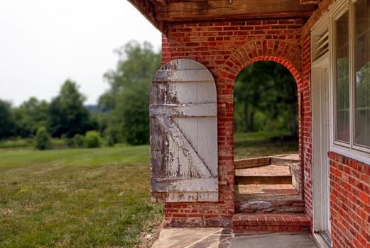 Ancient white painted door in bright red brick wall opening onto garden and trees