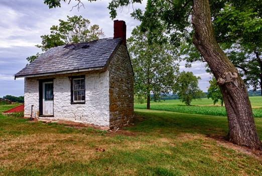 Old stone white washed cottage on farmland with trees and plants in the background. Slate roof