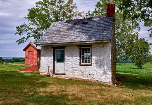 Old stone white washed cottage on farmland with trees and plants in the background. Slate roof