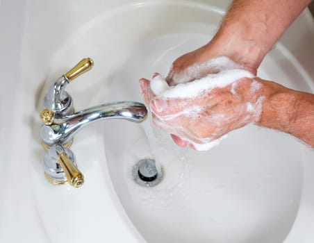 Senior man washing hands in modern sink with soap and lathering suds