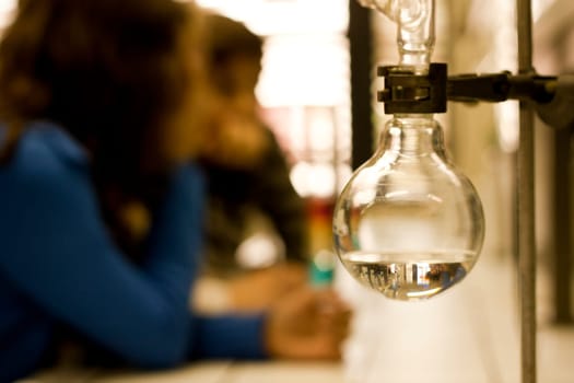 Focus on some chemistry equipment with students faded on the background.