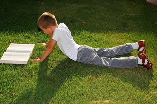 Young boy outdoors on the grass reading a book