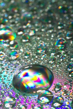 Close up view of many colorful and bright drops of water on a shiny surface.